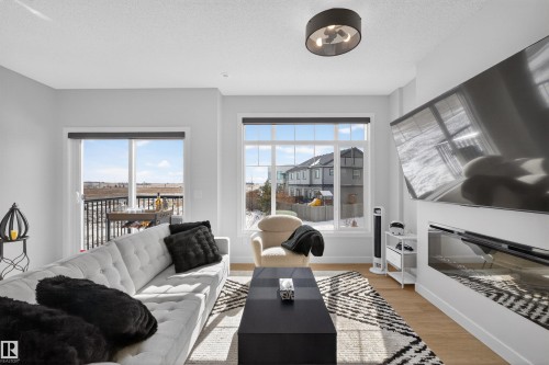 Bright living area with large windows, a sliding glass door leading to a balcony, and light-colored flooring - 28 6214 Cartmell Crest, Edmonton, AB - Indoor Photo Showing Living Room With Fireplace