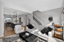 Open-concept living area with light wood-finish flooring, featuring a kitchen island with seating, pendant lighting fixtures, a modern staircase with dark metal balusters, and a large window providing natural light - 28 6214 Cartmell Crest, Edmonton, AB  - Indoor 