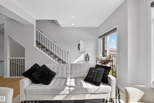 Living room featuring a light-colored sofa, large windows, and an open staircase with black railings - 28 6214 Cartmell Crest, Edmonton, AB - Indoor