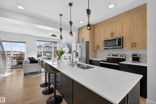 Open concept kitchen featuring a large island with seating, stainless steel appliances, and light wood cabinetry - 28 6214 Cartmell Crest, Edmonton, AB - Indoor Photo Showing Kitchen With Double Sink With Upgraded Kitchen
