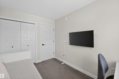 This room features a neutral color palette, carpeted flooring, and a modern paneled door with black hardware - 28 6214 Cartmell Crest, Edmonton, AB - Indoor