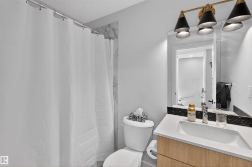 Well-appointed bathroom featuring a vanity with a white countertop, a mirror, and a modern light fixture with three conical shades - 28 6214 Cartmell Crest, Edmonton, AB - Indoor Photo Showing Bathroom