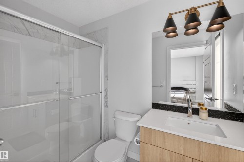 The bathroom features a sleek vanity with a light wood-toned base, a white countertop, and a dark speckled backsplash - 28 6214 Cartmell Crest, Edmonton, AB - Indoor Photo Showing Bathroom