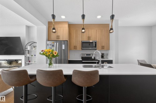 Open-concept kitchen featuring light-toned cabinetry, stainless steel appliances, and a large island with a sink and pendant lighting - 28 6214 Cartmell Crest, Edmonton, AB - Indoor Photo Showing Other Room