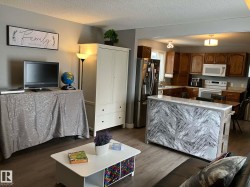 Open-concept living area with wood-finish flooring, a kitchen featuring wood cabinetry, stainless steel refrigerator, white range, and microwave - 