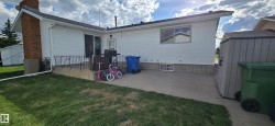 Rear exterior featuring white vinyl siding, a concrete patio, a brick chimney, and a storage shed - 