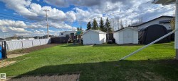 Expansive grassy yard featuring a white privacy fence, two white storage sheds, and a black fabric shelter - 