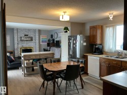 Open-concept kitchen featuring wood-finish flooring, dark wood cabinetry, stainless steel appliances, and a dining area with a wood table - 