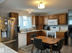 Kitchen featuring wood cabinetry, stainless steel refrigerator, white electric range with overhead microwave, double basin stainless steel sink, and light-toned countertops - 