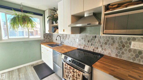 Kitchen featuring wood-finish countertops, a stainless steel sink with a gooseneck faucet, a patterned tile backsplash, white cabinetry, and a window - 3531 46 Street, Edmonton, AB - Indoor Photo Showing Kitchen With Double Sink