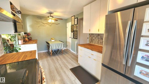 Modern kitchen featuring stainless steel appliances, light wood-finish flooring, white cabinetry with gold-tone hardware, and a mosaic tile backsplash - 3531 46 Street, Edmonton, AB - Indoor Photo Showing Kitchen