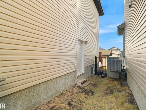 Exterior side entry featuring a white door with an integrated window, a wall-mounted exterior light fixture, and a chain-link fence at the rear - 5192 1B Avenue Sw, Edmonton, AB - Outdoor With Exterior