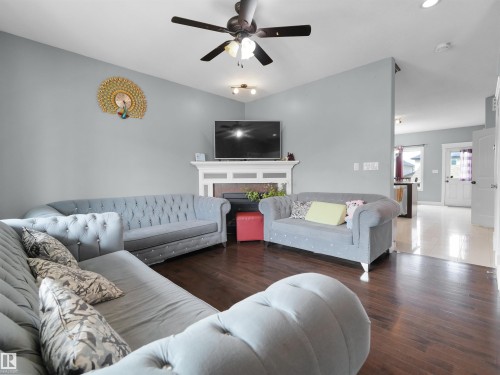 Living area featuring wood-finish flooring, a white mantel, and a ceiling fan - 5192 1B Avenue Sw, Edmonton, AB - Indoor Photo Showing Living Room With Fireplace