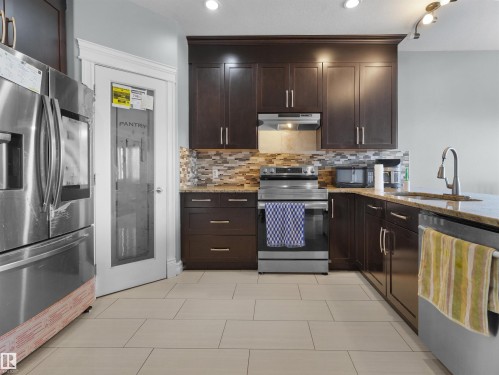 Kitchen featuring dark wood cabinetry, stainless steel appliances, a mosaic tile backsplash, and light-toned tile flooring - 5192 1B Avenue Sw, Edmonton, AB - Indoor Photo Showing Kitchen With Upgraded Kitchen