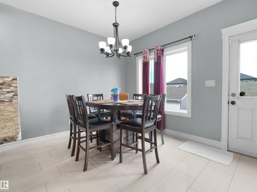 Dining area featuring light-toned tile flooring, a multi-light chandelier, a window with white trim, and a white paneled door - 5192 1B Avenue Sw, Edmonton, AB - Indoor Photo Showing Dining Room