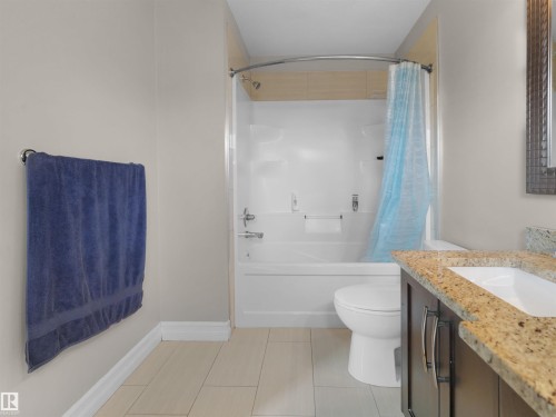 Bathroom featuring a spacious tub/shower combination, a vanity with a light-toned countertop, and wood-finish flooring - 5192 1B Avenue Sw, Edmonton, AB - Indoor Photo Showing Bathroom