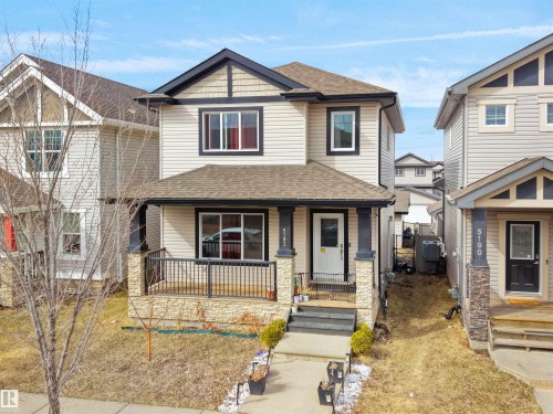 Two-story residence featuring light-colored siding, a covered front porch with stone-wrapped columns, and dark trim accents - 5192 1B Avenue Sw, Edmonton, AB - Outdoor With Deck Patio Veranda With Facade