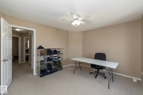 Carpeted room featuring a ceiling fan with integrated lighting, neutral wall paint, white baseboards, and a paneled interior door - 50 14803 Miller Boulevard, Edmonton, AB - Indoor