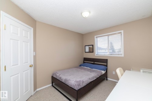 Carpeted room with neutral-toned walls, featuring a six-panel door with brass hardware and a window with horizontal blinds - 50 14803 Miller Boulevard, Edmonton, AB - Indoor Photo Showing Bedroom