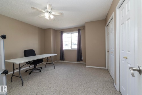 Carpeted room featuring neutral-toned walls, a double window with drapes, and two closet doors with gold-toned hardware - 50 14803 Miller Boulevard, Edmonton, AB - Indoor