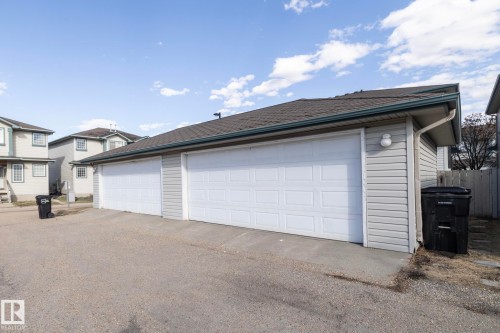 Detached multi-car garage with light gray horizontal vinyl siding, white paneled garage doors, dark shingle roofing, and a gravel driveway - 50 14803 Miller Boulevard, Edmonton, AB - Outdoor