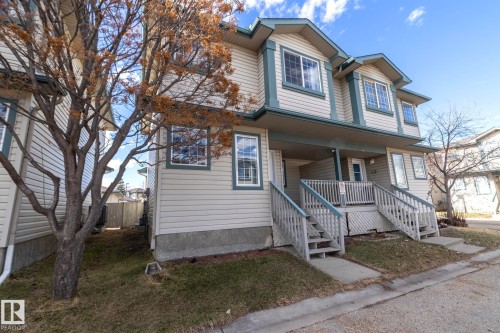 Multi-level townhouse exterior featuring light-colored siding with contrasting trim, multiple gabled dormers, a covered entryway with a porch, and dual exterior staircases - 50 14803 Miller Boulevard, Edmonton, AB - Outdoor