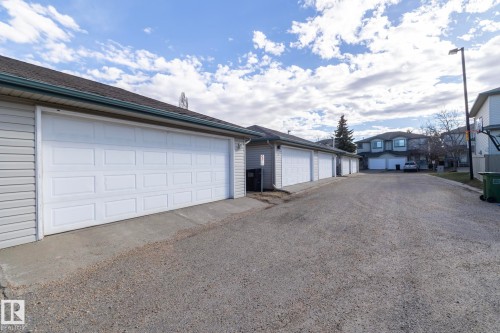 Multiple garage doors with panel detailing, light-toned siding, and dark shingle roofing - 50 14803 Miller Boulevard, Edmonton, AB - Outdoor