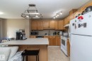 Kitchen featuring wood cabinetry, white appliances, track lighting, and a pot rack pendant light - 50 14803 Miller Boulevard, Edmonton, AB  - Indoor Photo Showing Kitchen With Double Sink 