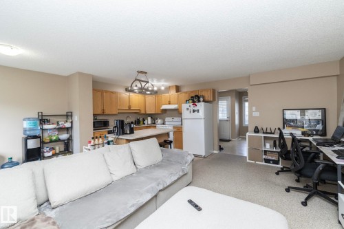 Open-concept living area featuring a kitchen with light wood cabinetry, white appliances, and a peninsula with countertop seating - 50 14803 Miller Boulevard, Edmonton, AB - Indoor Photo Showing Living Room