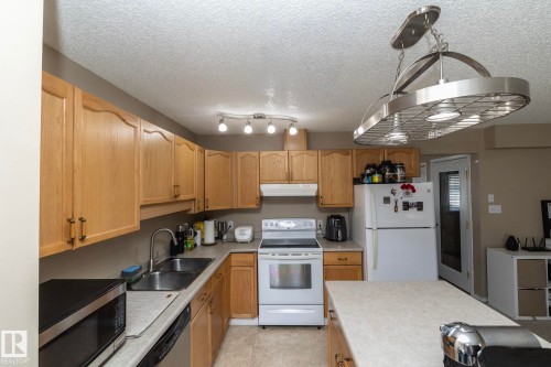 Kitchen featuring light wood cabinetry, a double basin sink, white appliances, and a central island with an overhead lighting fixture - 50 14803 Miller Boulevard, Edmonton, AB - Indoor Photo Showing Kitchen With Double Sink