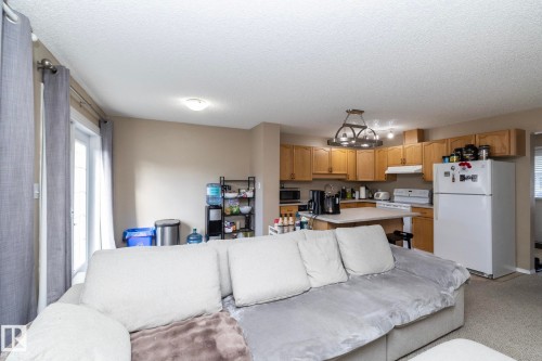 Open-concept living space featuring a kitchen with wood cabinetry, a white refrigerator, a white range, and an island with a light-colored countertop - 50 14803 Miller Boulevard, Edmonton, AB - Indoor