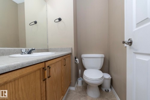 Bathroom featuring a vanity with a light-toned countertop, an integrated sink, and wood-finish cabinetry with dark hardware - 50 14803 Miller Boulevard, Edmonton, AB - Indoor Photo Showing Bathroom