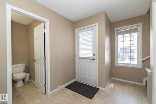 Entryway featuring neutral wall paint, tile flooring, a white paneled door, and a white-framed window with blinds - 50 14803 Miller Boulevard, Edmonton, AB - Indoor