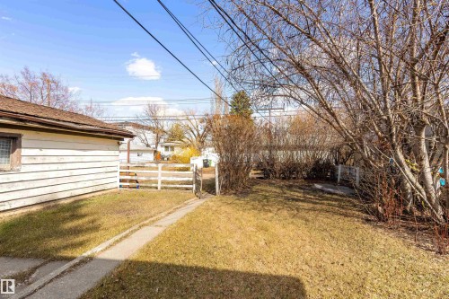 Expansive backyard featuring a white picket fence, mature trees, and a concrete pathway leading to a detached structure with horizontal siding and a shingle roof - 9007 149 Street, Edmonton, AB - Outdoor With View
