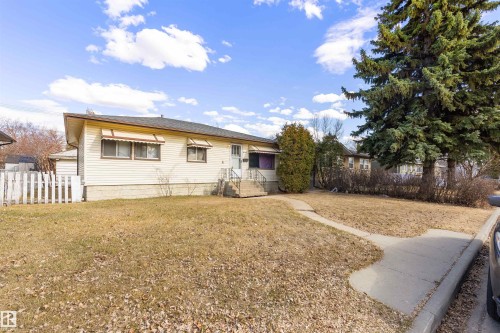 Single-story residence featuring light-colored siding, a dark shingle roof, and a mature evergreen tree - 9007 149 Street, Edmonton, AB - Outdoor
