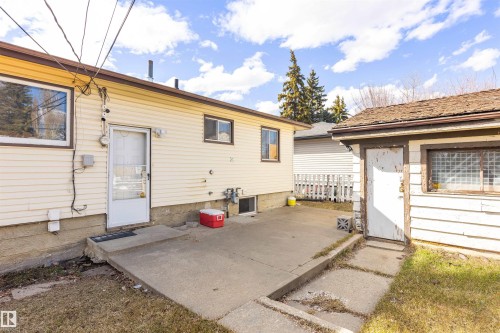 Rear exterior featuring light-colored horizontal siding, a concrete patio, and an adjacent auxiliary building with horizontal siding and a window - 9007 149 Street, Edmonton, AB - Outdoor With Exterior