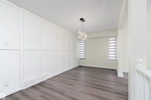 The property features a room with a white paneled accent wall, wood-look flooring, and a modern light fixture - 11020 158 Avenue, Edmonton, AB - Indoor Photo Showing Other Room