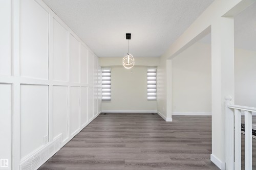 An open concept living area featuring grey hardwood floors, a modern light fixture, and two windows with blinds - 11020 158 Avenue, Edmonton, AB - Indoor Photo Showing Other Room