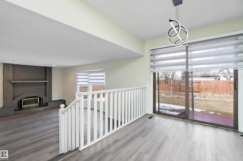 Spacious living area featuring light-toned flooring, a staircase with white railings, a brick fireplace, and sliding glass doors leading to the outdoor area - 11020 158 Avenue, Edmonton, AB - Indoor Photo Showing Other Room