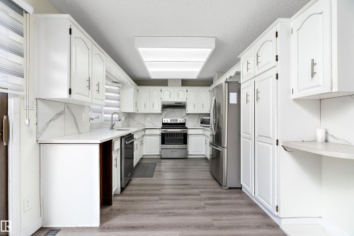 The kitchen features extensive white cabinetry, light-colored countertops, and stainless steel appliances including a refrigerator, oven, and dishwasher - 11020 158 Avenue, Edmonton, AB - Indoor Photo Showing Kitchen