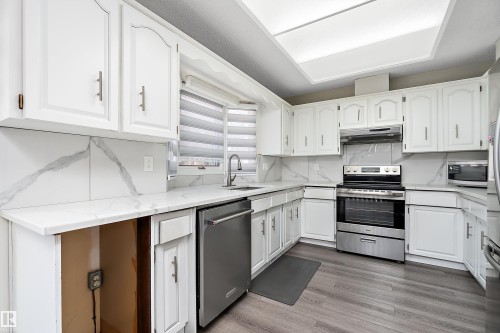 The kitchen features white cabinetry, white countertops, and stainless steel appliances, including a range and a dishwasher - 11020 158 Avenue, Edmonton, AB - Indoor Photo Showing Kitchen