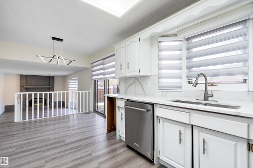 The kitchen features white cabinetry, a stainless steel dishwasher, a stainless steel sink with a gooseneck faucet, and windows with blinds - 11020 158 Avenue, Edmonton, AB - Indoor Photo Showing Kitchen With Double Sink