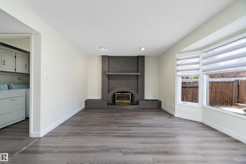 This inviting living area features hardwood style flooring, a bay window with blinds, and a brick fireplace - 11020 158 Avenue, Edmonton, AB - Indoor With Fireplace