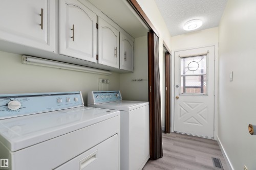 This functional utility area features white cabinetry, a washer and dryer, and durable vinyl flooring - 11020 158 Avenue, Edmonton, AB - Indoor Photo Showing Laundry Room