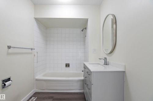 The bathroom features a bathtub with white tile surround, a modern vanity with a white countertop, and a sleek oval mirror - 11020 158 Avenue, Edmonton, AB - Indoor Photo Showing Bathroom