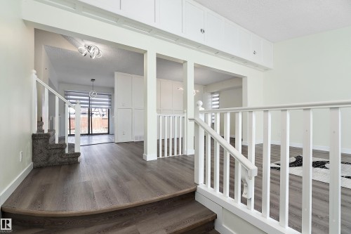 The property features durable wood-look flooring throughout, a carpeted staircase with white railings, and white built-in cabinetry - 11020 158 Avenue, Edmonton, AB - Indoor Photo Showing Other Room