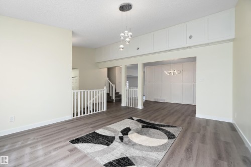 Spacious interior with light-colored walls and grey flooring, featuring a modern chandelier and white railings - 11020 158 Avenue, Edmonton, AB - Indoor