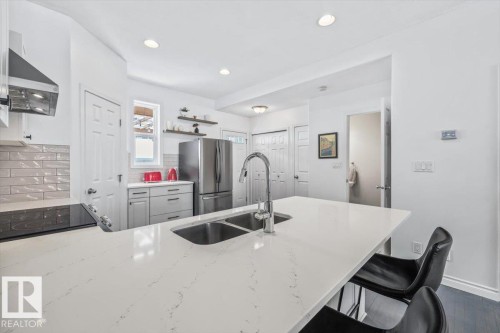 Modern kitchen featuring a white countertop island with a double sink, stainless steel appliances, and sleek grey subway tile backsplash - 8737 83 Avenue, Edmonton, AB - Indoor Photo Showing Kitchen With Double Sink