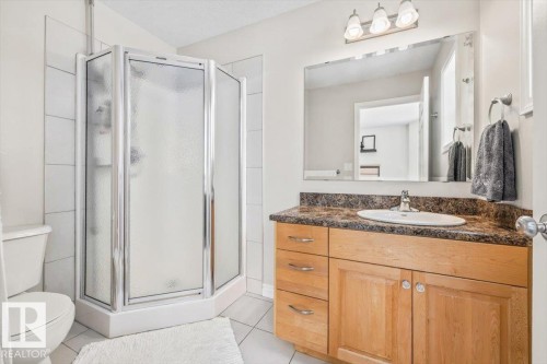 The bathroom features a corner shower with a clear and frosted glass enclosure, a toilet, and a vanity with a light wood finish - 8737 83 Avenue, Edmonton, AB - Indoor Photo Showing Bathroom