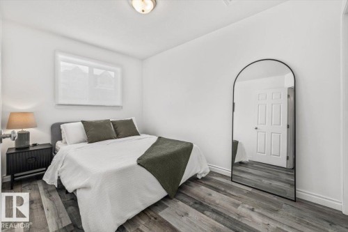The bedroom features light-coloured walls, wood-style flooring, and a window with white blinds - 8737 83 Avenue, Edmonton, AB - Indoor Photo Showing Bedroom